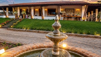 Un patio con una fuente, un edificio con techo de tejas y un césped bien cuidado.