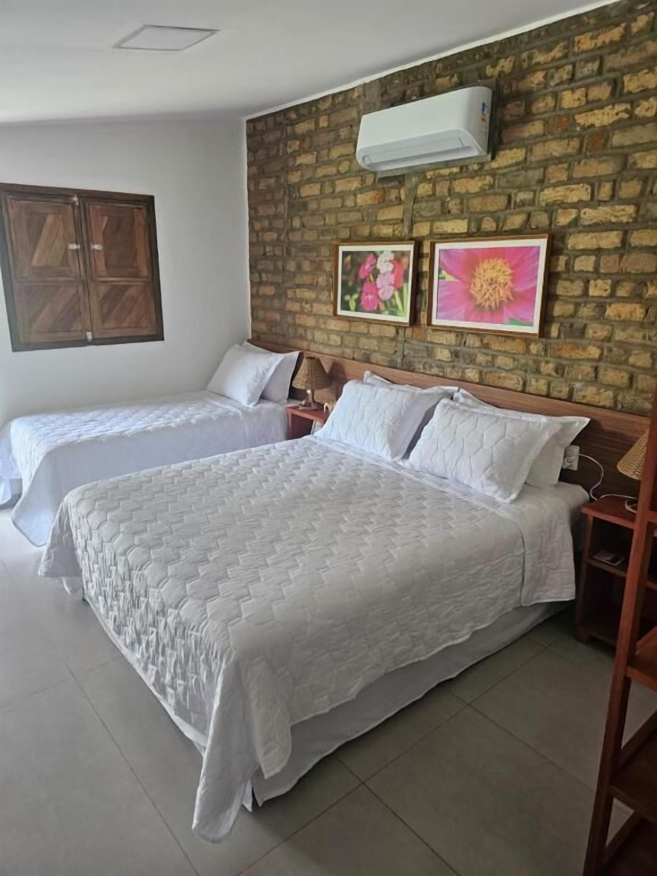 A hotel room with two beds, a brick wall, and a window.