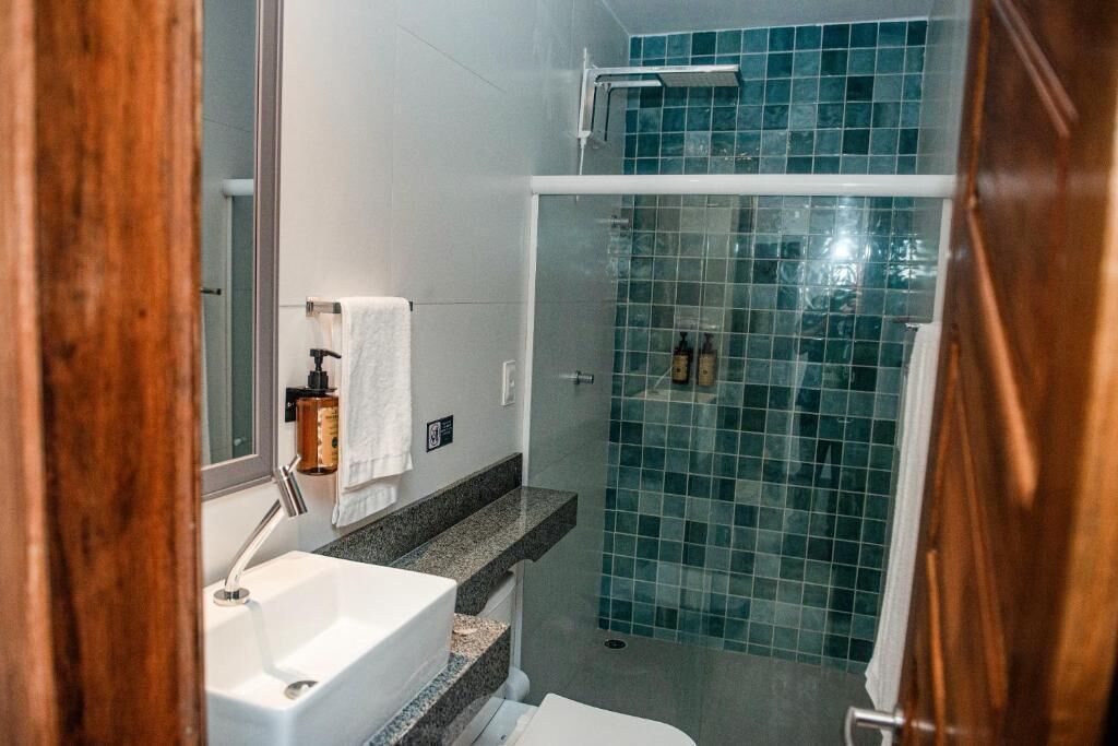 A bathroom with a white sink, a mirror, a towel, and a shower with blue-tiled walls.