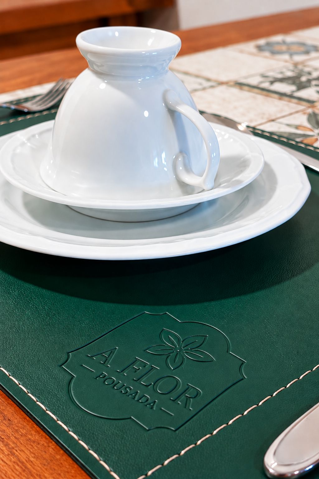 Un juego de tetera y taza blancos sobre un mantel verde con texto en relieve.