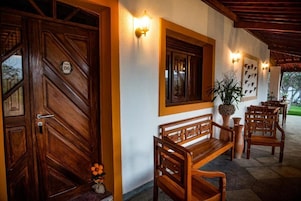 Uma porta de madeira com placa de número, um banco e luminárias fixadas na parede.