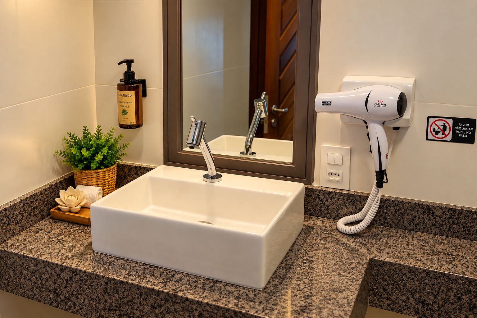 Un baño con lavamanos blanco, secador de pelo, botella de champú y una planta.