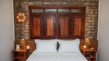 Quarto com grande cabeceira de madeira, cama com roupa de cama branca, duas mesas de cabeceira com abajures e um relógio de parede.