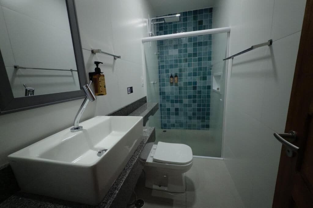 Casa de banho com lavatório branco, sanita e zona de duche com cabine de vidro.