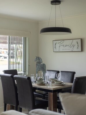 A dining area with a table set for four, chairs, a pendant light, and a framed sign on the wall. - Great Value | Private Pool| Walk to Market Square (Sunnybank)