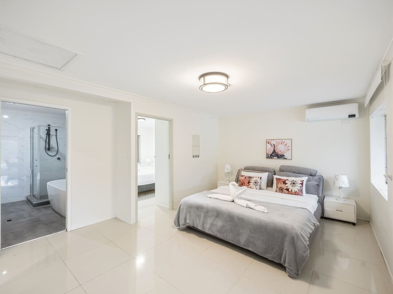 A modern bedroom with a large bed, bedside tables, a nightstand, and a window.
