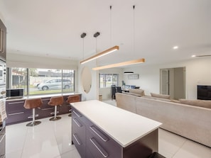 A modern kitchen with a central island, bar stools, and a dining area with a sofa. - Great Value | Private Pool| Walk to Market Square (Sunnybank)