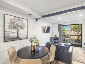 Un salon moderne avec une table ronde, des canapés, un téléviseur à écran plat fixé au mur et une vue sur l’extérieur grâce à une porte-fenêtre coulissante.