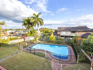 Ein rechteckiger Swimmingpool mit schwarzem Metallzaun, umgeben von Rasenfläche und einer Holzterrasse.