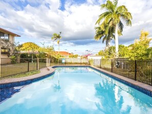 A swimming pool with a tiled edge, surrounded by a fence, and palm trees in the background. - Great value Sunnybank Family Stay | Pool | Parking (Sunnybank)