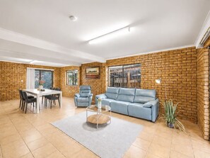 Ein geräumiges Wohnzimmer mit Backsteinwand, einem weißen Esstisch mit Stühlen, einem blauen Sofa und einem Couchtisch.