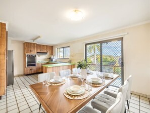 A modern kitchen with wooden cabinets, a dining table set for six, and a sliding glass door leading to a balcony. - Great value Sunnybank Family Stay | Pool | Parking (Sunnybank)