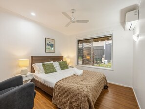 Ein Schlafzimmer mit Bett, Nachttischlampen, Deckenventilator, Fenster mit Aussicht und einer Wand-Klimaanlage.