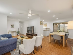 Uma sala de estar moderna com sofá, cadeiras, televisão e mesa de jantar.