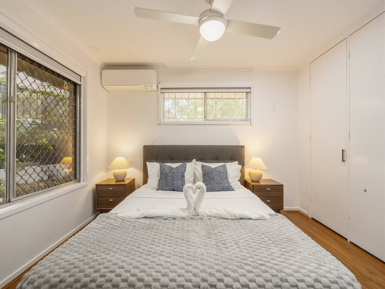 Una camera da letto con un letto, due comodini, una ventola a soffitto, un condizionatore d'aria, una finestra con vista e un armadio.