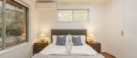Un dormitorio con cama, dos mesitas de noche, ventilador de techo, aire acondicionado, ventana con vistas y armario.