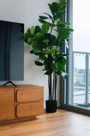 A modern living room with a wooden cabinet, a large flat-screen TV, and a tall potted plant by a window. - Central Locate|City View| Walk to South Bank & CBD (South Brisbane)