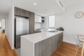 A modern kitchen with a central island, stainless steel appliances, and a dining area with a table and chairs. - Central Locate|City View| Walk to South Bank & CBD (South Brisbane)