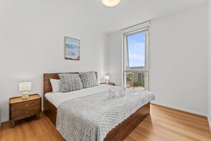 A bedroom with a large window, a bed with a grey blanket, a bedside table with a lamp, and a framed picture on the wall. - Central Locate|City View| Walk to South Bank & CBD (South Brisbane)