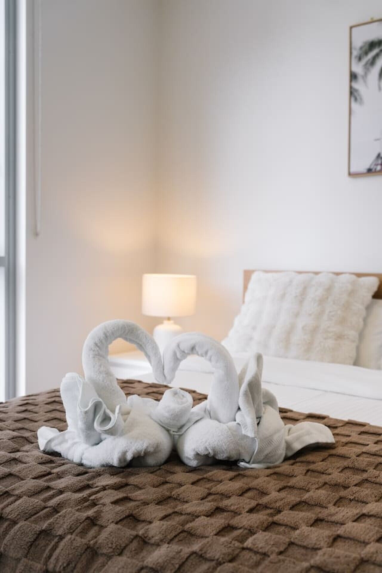 A bed with a brown textured blanket, a white pillow, and a lamp on a bedside table.