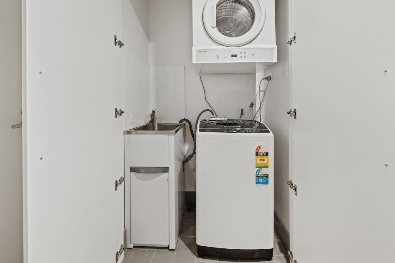A compact laundry room with a washing machine and a dryer, both white, with visible energy and water rating stickers.