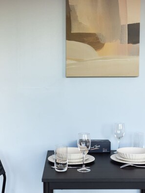 Een eettafel gedekt met borden, glazen en bestek, tegen een lichtblauwe muur met daarboven een groot abstract schilderij.