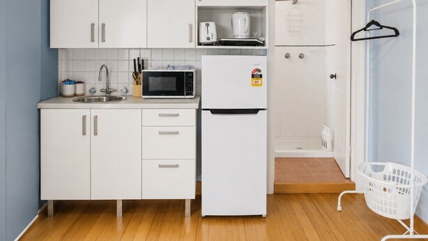 A compact kitchen with white cabinets, a microwave, a toaster, and a refrigerator.