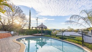 Una piscina de borde curvo, rodeada por una valla y un pabellón al fondo.