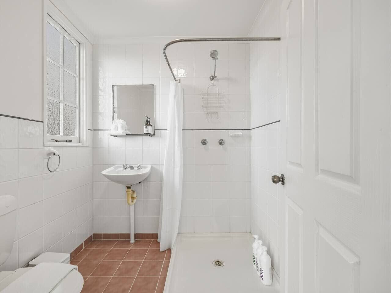 Une salle de bain avec un lavabo blanc, un miroir, une douche avec une porte en verre et des toilettes.