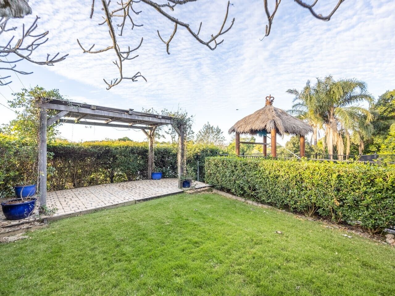 Een tuin met een pergola, een constructie met rieten dak en goed onderhouden hagen.