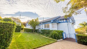 Una casa de dos pisos con fachada azul y blanca, un césped cuidado y un cielo despejado.
