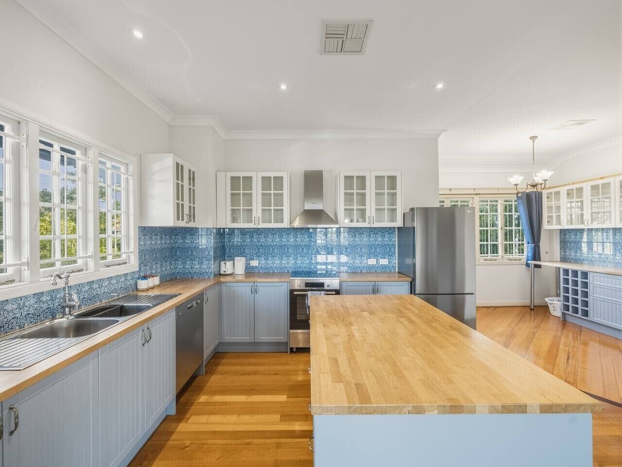 A modern kitchen with a central island, built-in appliances, and a blue-tiled backsplash.