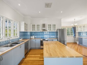 A modern kitchen with a central island, built-in appliances, and a blue-tiled backsplash. - Character Home| Mt Coot-tha Views | Prime location (Sherwood)