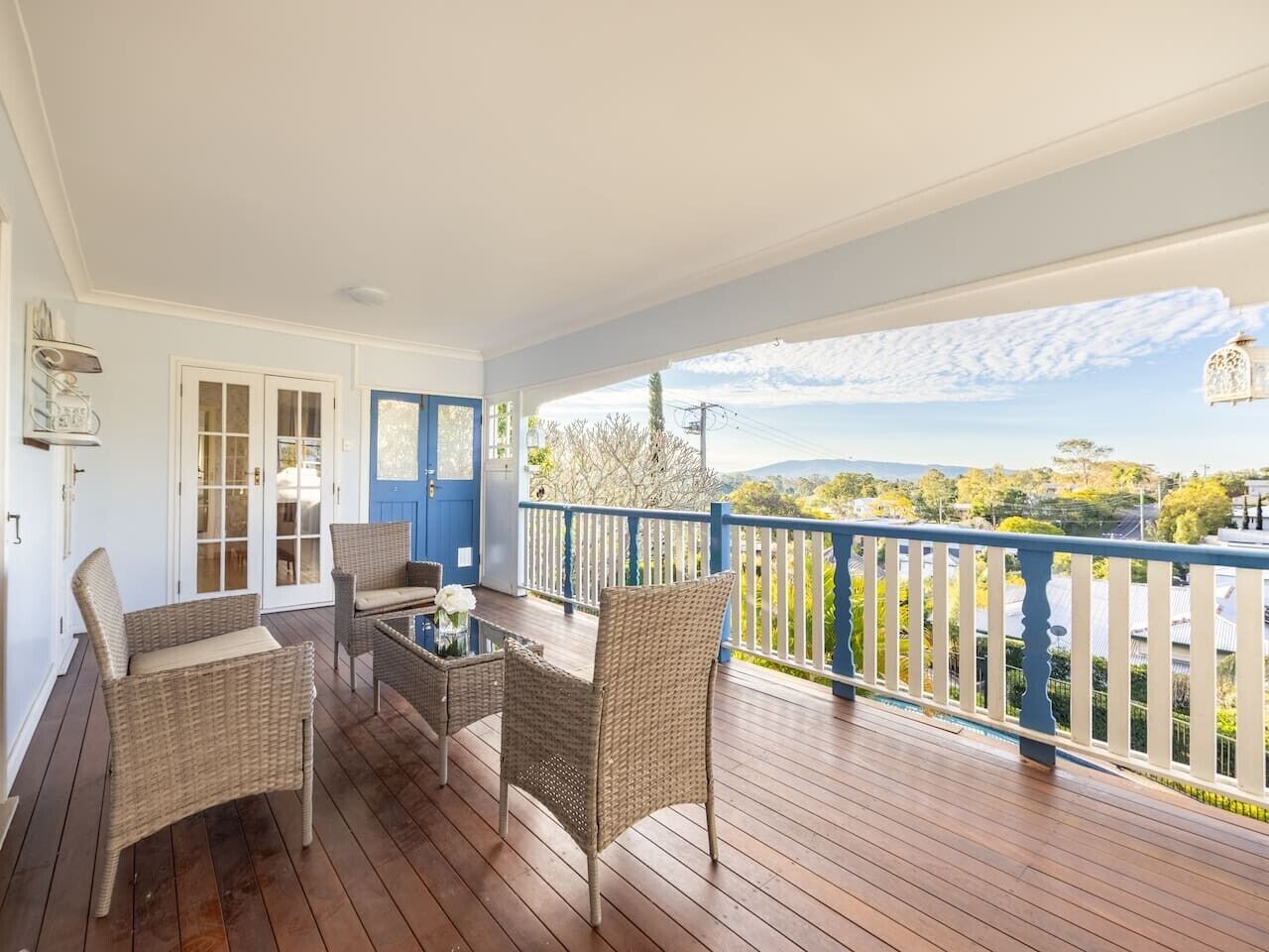 A covered porch with wicker furniture, a glass table, and a view of a landscape with trees and hills.