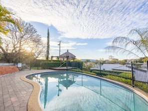 A swimming pool with a curved edge, surrounded by a fence, and a gazebo in the background. - Character Home| Mt Coot-tha Views | Prime location (Sherwood)
