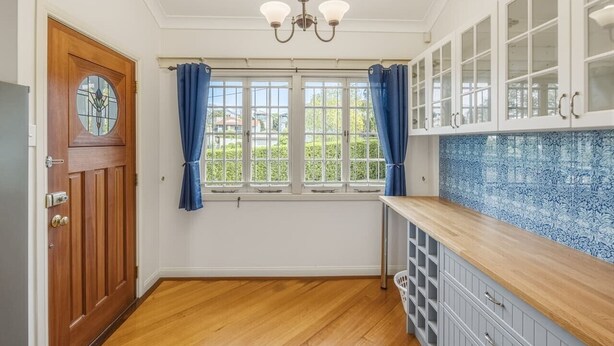 Una cocina con puerta de madera, una ventana con cortinas, una araña y armarios con un salpicadero de diseño azulado.