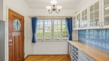 A kitchen with a wooden door, a window with curtains, a chandelier, and cabinets with a blue patterned backsplash.