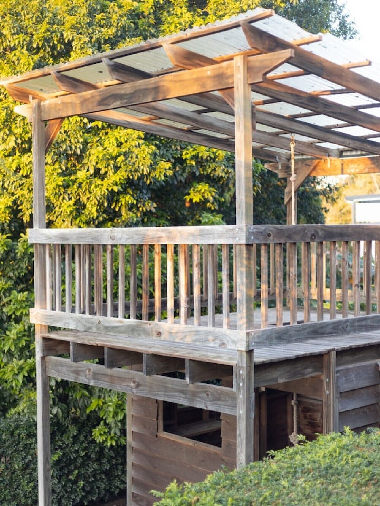 A wooden deck with a pergola structure, surrounded by greenery.