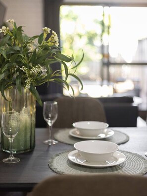 Une table à manger est dressée avec de l’assiette blanche, des bols et un verre. Un vase contenant des feuilles vertes et des fleurs blanches est posé sur la table.