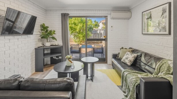 A modern living room with a sofa, a coffee table, a TV, and a balcony with outdoor furniture. - GreatValue Stay| Pool | Parking | Prime Location (Eight Mile Plains)