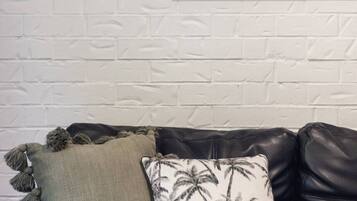 A black leather sofa with two decorative pillows against a white brick wall.