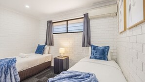 A hotel room with two beds, a nightstand, a window with curtains, and a white brick wall. - GreatValue Stay| Pool | Parking | Prime Location (Eight Mile Plains)
