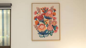 A room with a bed, a window with blinds, and a framed floral artwork on the wall.