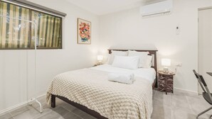 A bedroom with a bed, bedside tables, a window with blinds, an air conditioning unit, and a wall-mounted artwork. - Great Value Studio |Fully Renovated|Prime Location (Robertson)