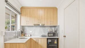 A compact kitchen with wooden cabinets, a microwave, a coffee maker, and a sink. - Great Value Studio |Fully Renovated|Prime Location (Robertson)