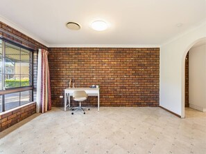 Um quarto com parede de tijolos, uma escrivaninha com cadeira, janela com cortinas e uma porta.