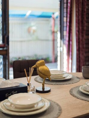 A dining table with a decorative bird centerpiece, multiple plates, and a glass candle holder. - Affordable Stay | Near Sunnybank |Prime Location (Robertson)