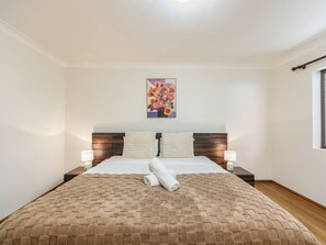 Ett hotellrum med en stor säng, två sänglampor, en sänggavel och ett konstverk som hänger på väggen.