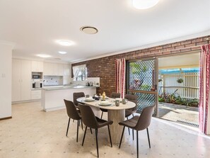 Een moderne keuken met witte kasten, een centraal eiland en een eethoek met stoelen.