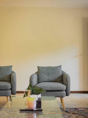 A room with two grey armchairs, a glass coffee table, and a potted plant. - Affordable Stay | Near Sunnybank |Prime Location (Robertson)